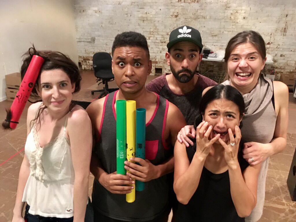 5 people stand huddled together to pose for a silly picture in rehearsals.