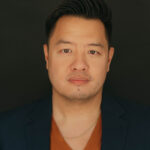 Headshot image of Kevin Wong. Kevin is wearing an orange v-neck shirt under a black suit jacket.