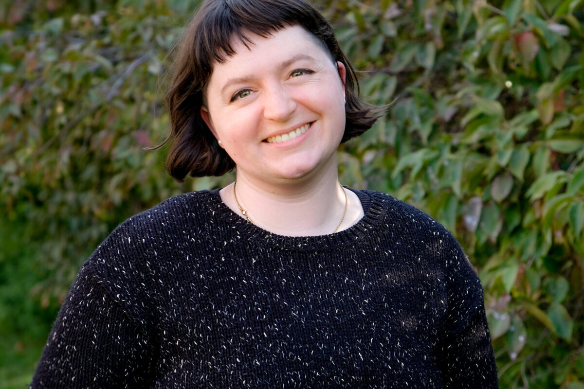 Photo of Lucy. Lucy is smiling, has short hair and is wearing a pullover sweater.