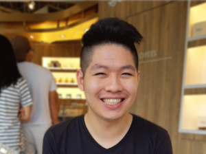 Photo of Ian Chan. Ian has black hair and brown eyes, wears a black t-shirt sitting in a coffee shop, and is smiling and looking at the camera.